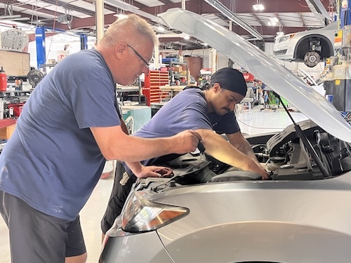 Two technicians working on a European car under the hood.